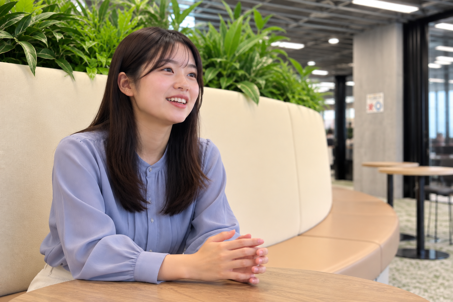 笑顔の若い女性と緑豊かなオフィスラウンジ.png